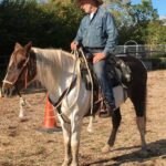 Photo of a man mounted on a skewbald coloured horse in an outdoor arena