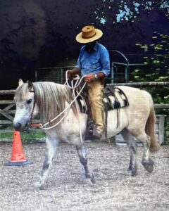Photo of a man riding a small dappled grey pony around an outdoor arena