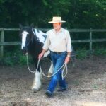 Photo of a man with a pony walking on a lead around the outskirts of an outdoor arena